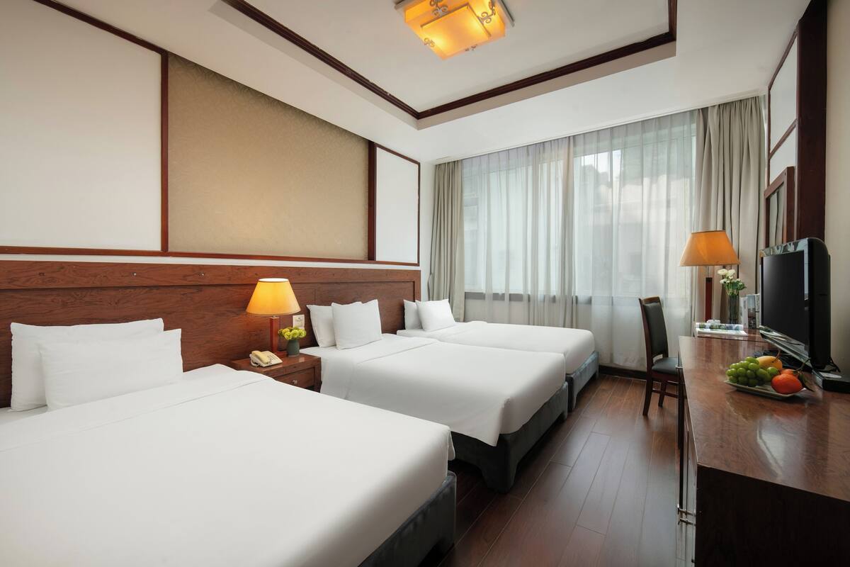 Ein Hotelzimmer mit zwei Betten, einem Schreibtisch mit Lampe, einem Fernseher und einer Obstschale.
