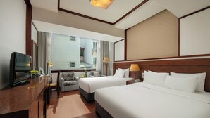Habitación de hotel con dos camas, un escritorio con televisor, un sofá y un amplio ventanal con vistas al exterior.