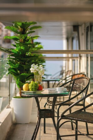 A balcony with a table set for two, featuring a potted plant, a vase with flowers, and a plate with fruits and a coffee cup. - Sao Mai Boutique Hotel (Hanoi)