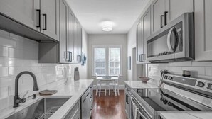 A modern kitchen with white cabinets, stainless steel appliances, and a wooden floor.