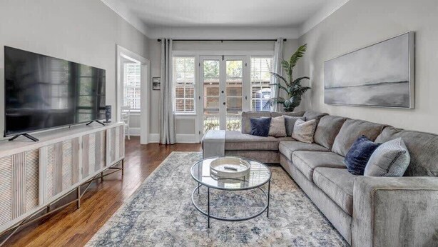 A modern living room with a large flat-screen TV, a grey sofa, a glass coffee table, and a ceiling fan.