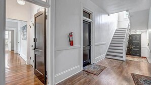 A hallway with wooden flooring, white walls, and a staircase leading to an upper level.
