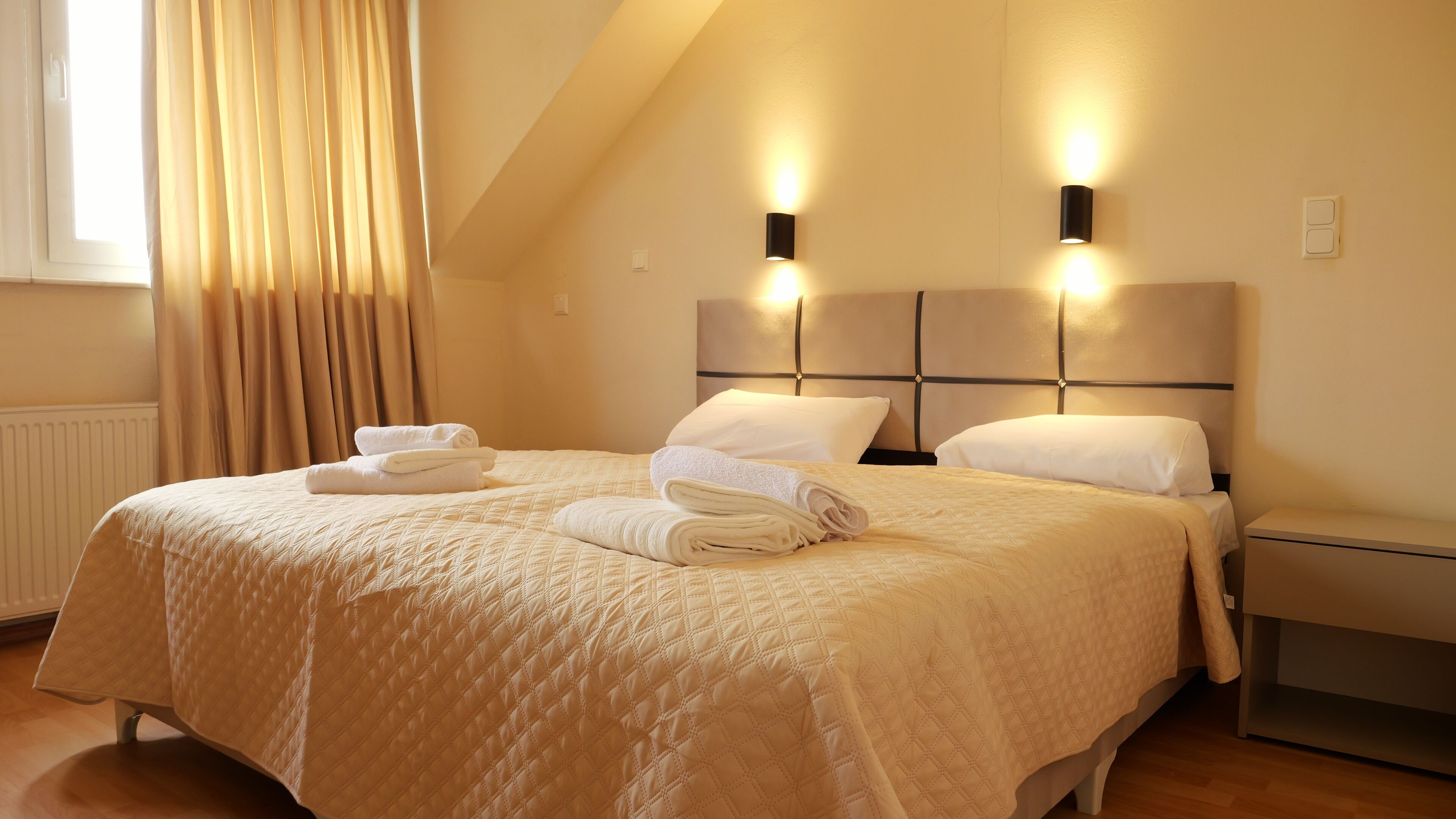 A neatly made bed with a quilted duvet, two pillows, and folded towels on a headboard.