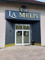 Fachada de um edifício com uma placa que diz "LA MELIS" e um logotipo acima da entrada.