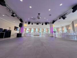 Um salão amplo com palco, mesas e cadeiras dispostas para um evento.
