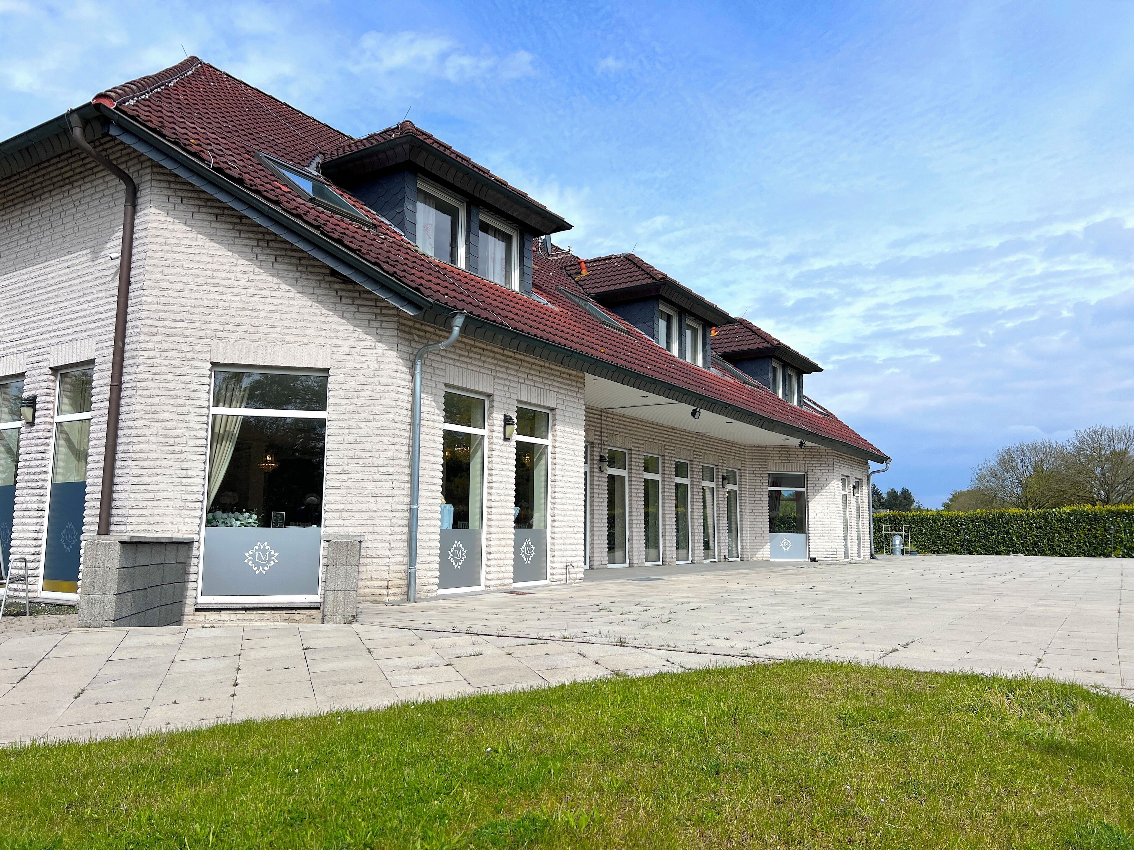 A two-story building with a red-tiled roof, large windows, and a paved driveway.