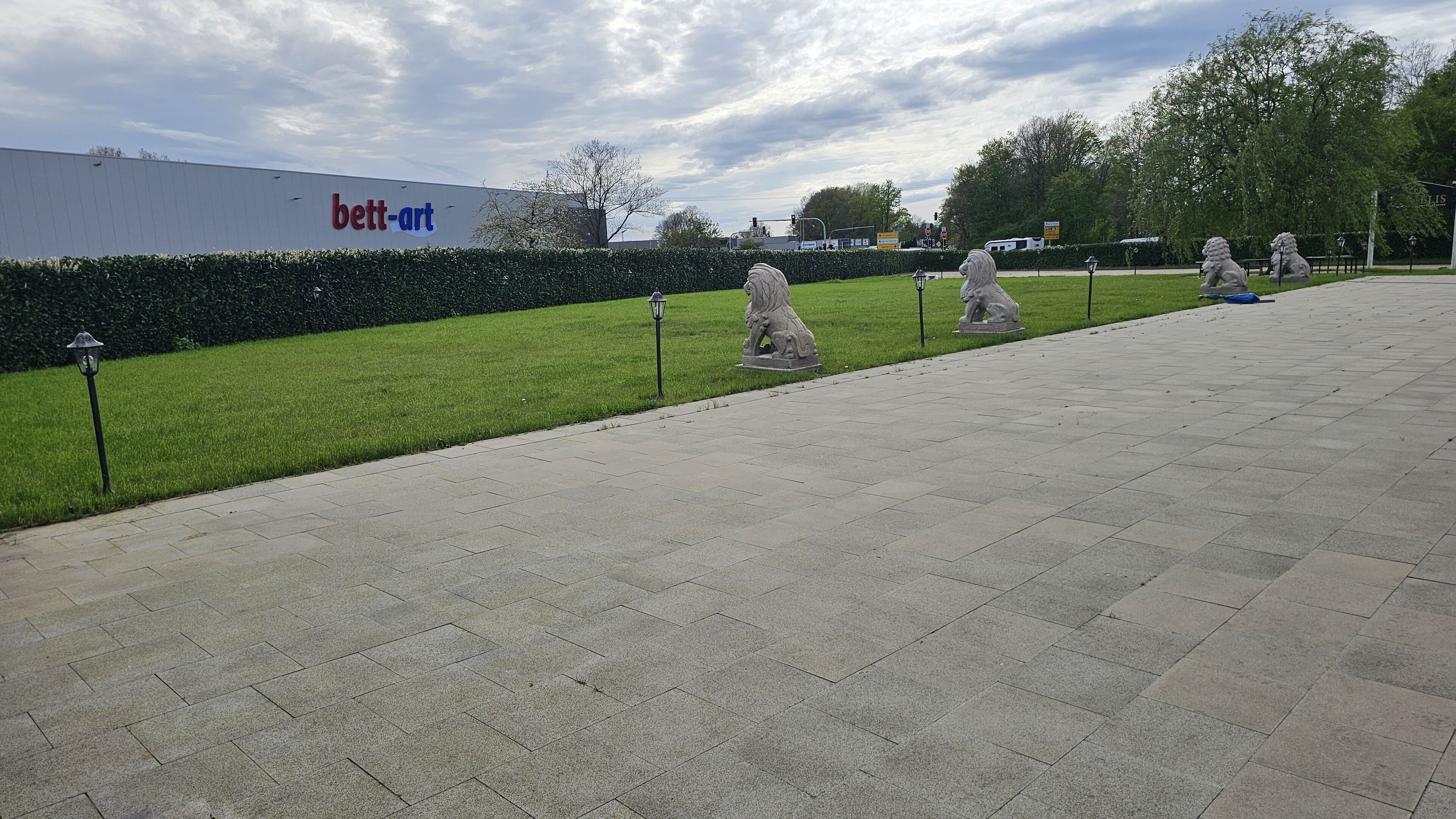 A paved walkway with stone tiles, a hedge, and a statue of a lion.