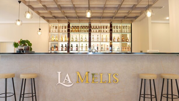 A bar area with a marble countertop, bar stools, and a variety of bottles displayed in the background. - La Melis  (Geldern)