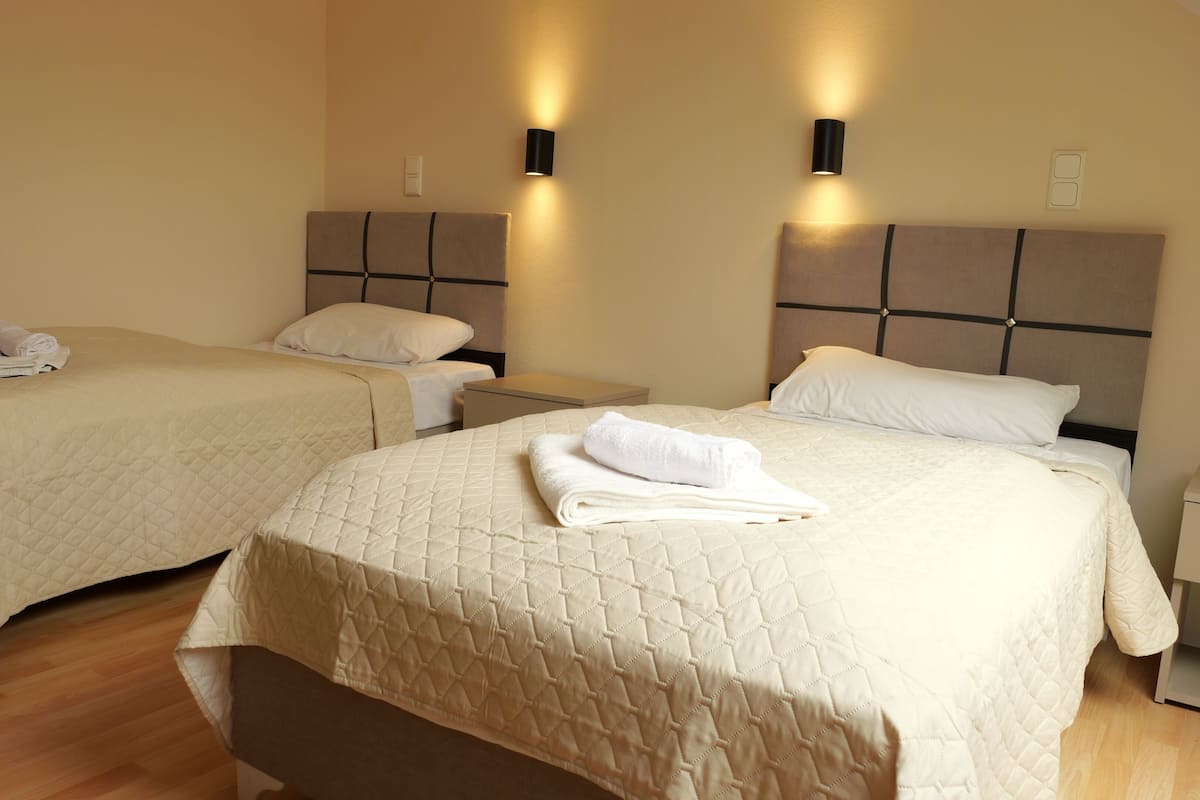 A hotel room with two beds, each with a headboard, bedside tables, and a folded towel on the beds.