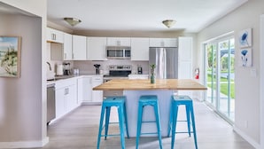 A modern kitchen with white cabinets, stainless steel appliances, and a central island with bar stools. - Elegant 2BR Haven by the Water (Riviera Beach)