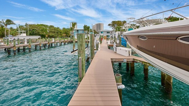 A marina with wooden docks extending into clear blue water, surrounded by greenery and buildings. - Elegant 2BR Haven by the Water (Riviera Beach)