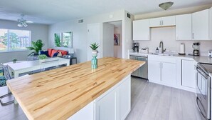 Una cuina moderna amb armaris blancs, tauleig de fusta i zona de menjador amb taula i cadires blanques.