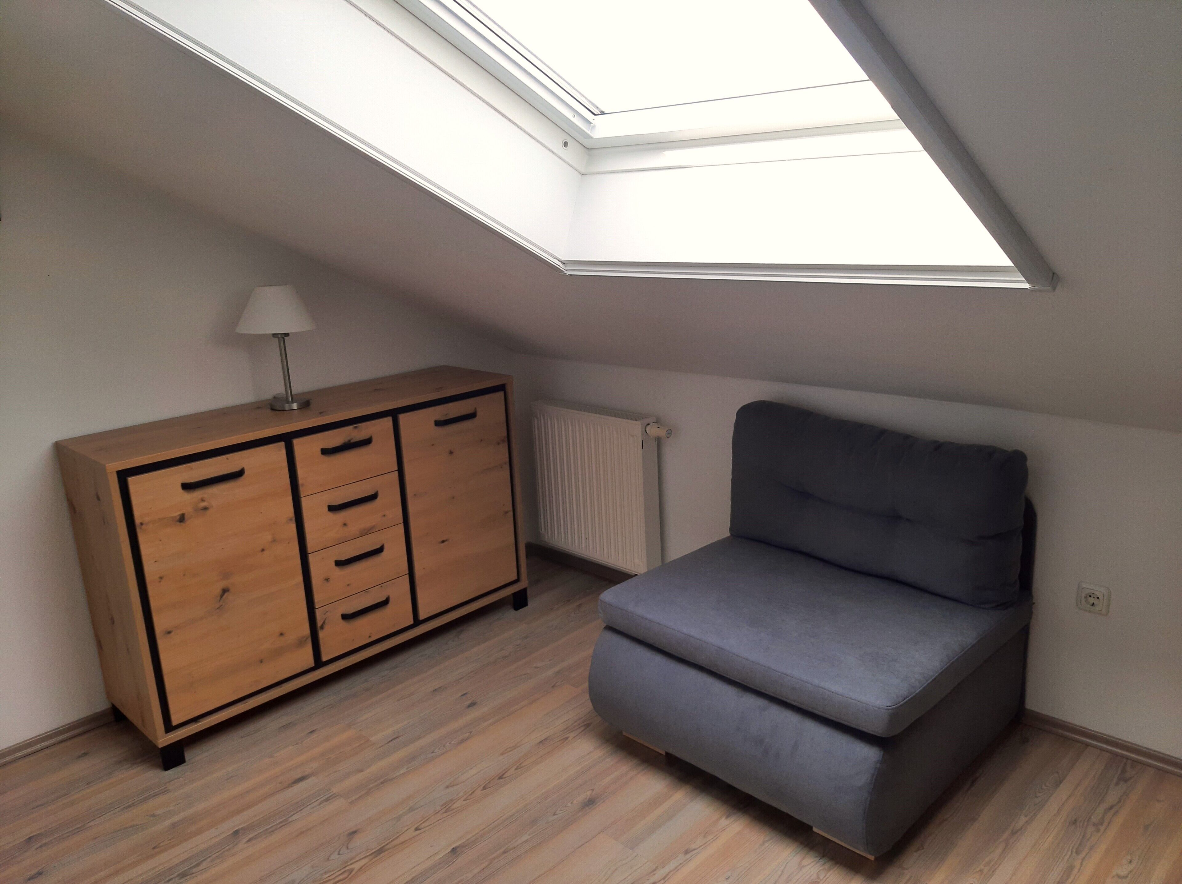 Ein Zimmer mit einer Dachfenster, einem Holzschrank und einem grauen Sofa.
