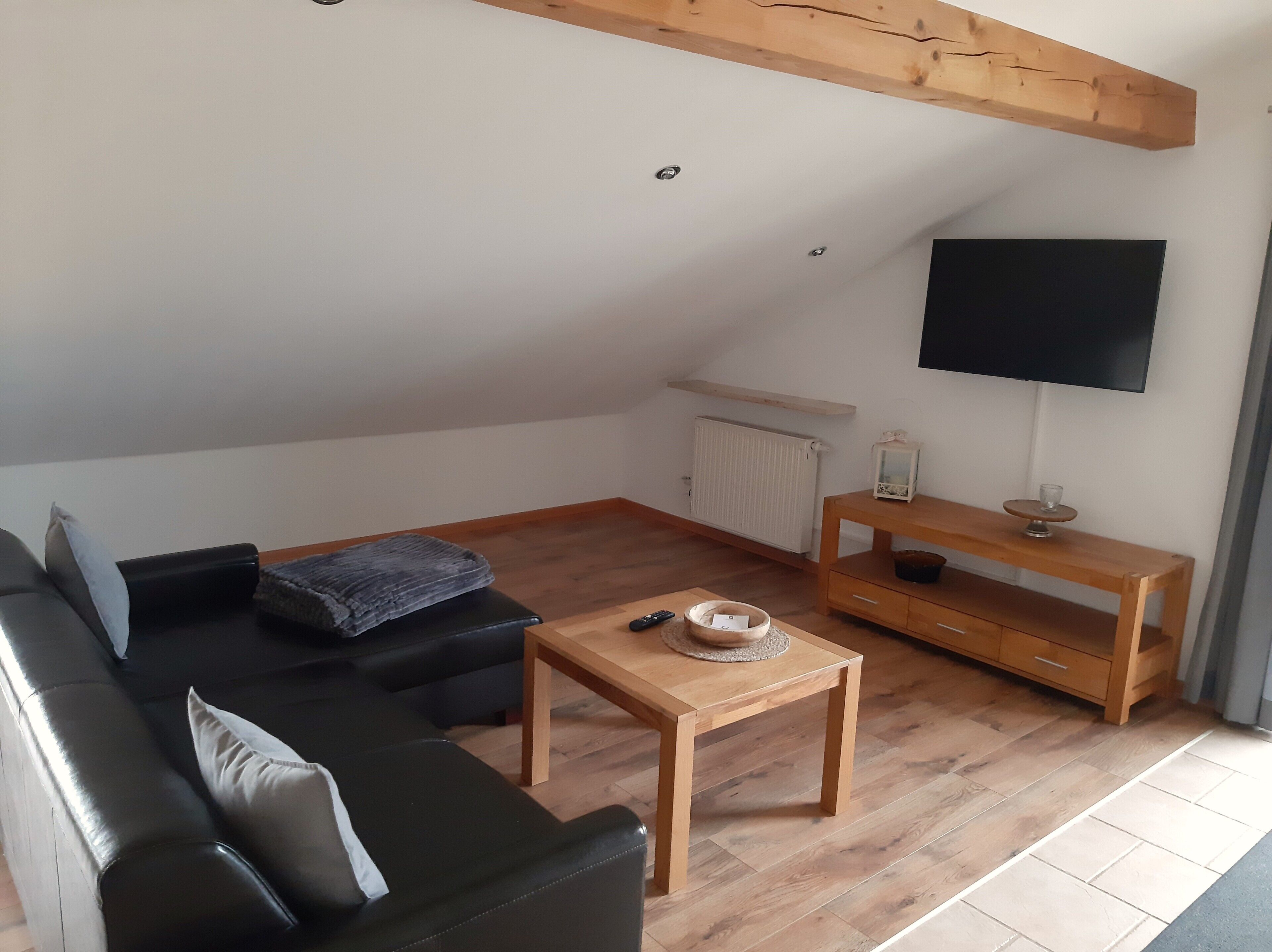 Een moderne loftkamer met een leren bank in het zwart, een houten salontafel, een houten tv-meubel en een witte radiator.