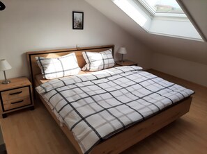 Une chambre à coucher avec un lit en bois, deux tables de chevet, une lampe de chevet, un tableau encadré au mur et une lucarne.