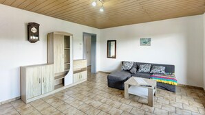 A room with a wooden ceiling, a sofa with a colorful blanket, a wooden cabinet, and a clock on the wall.