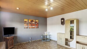A living room with a flat-screen TV, wooden cabinets, a glass coffee table, and wall-mounted artwork.