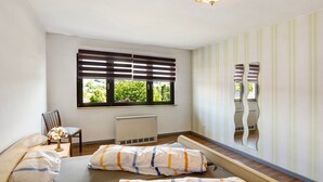 A room with a bed, a chair, a radiator, a window with blinds, and a mirror with a wavy design.