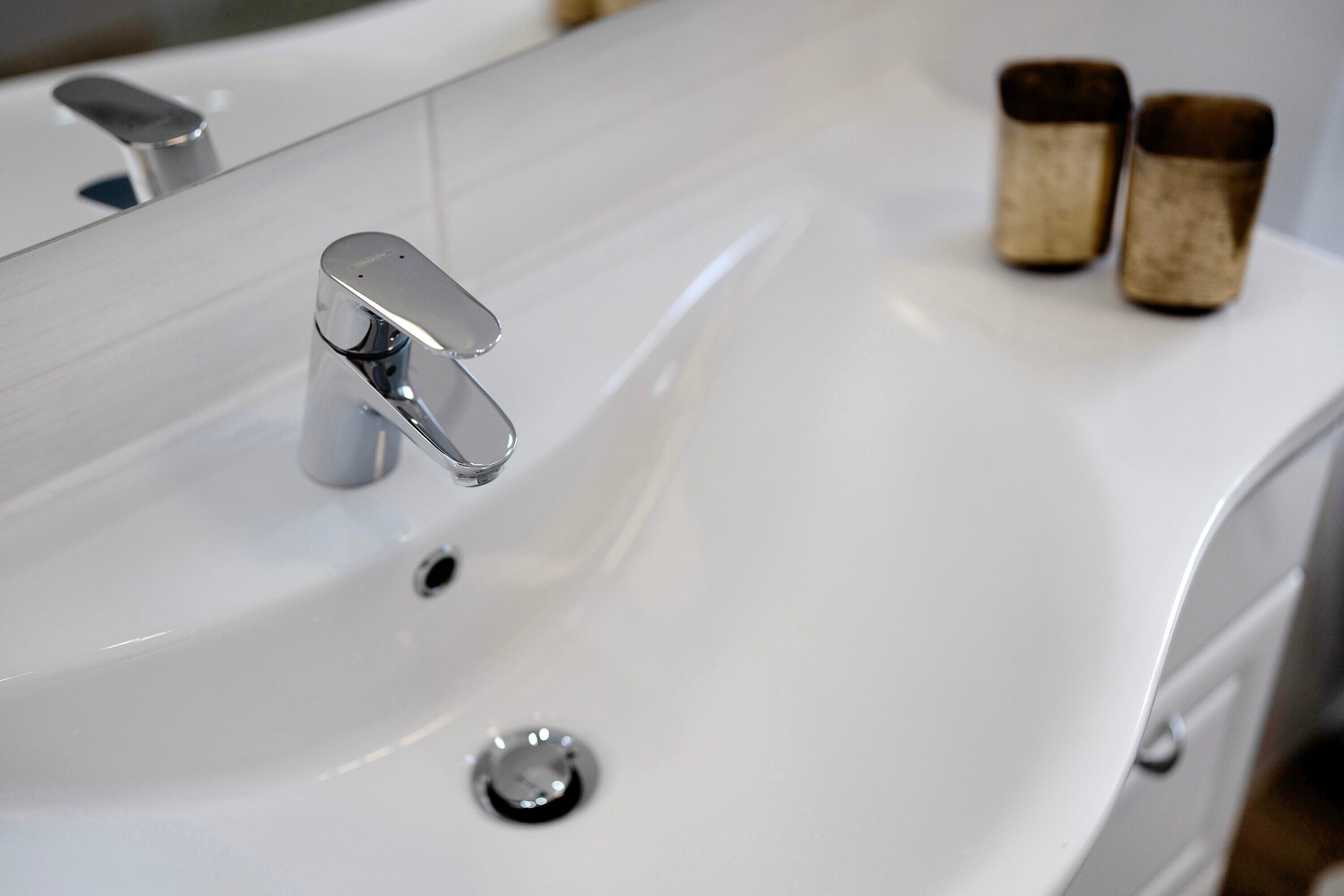 Un lavabo blanc dans une salle de bain, doté d'un robinet moderne et d'un miroir au-dessus.