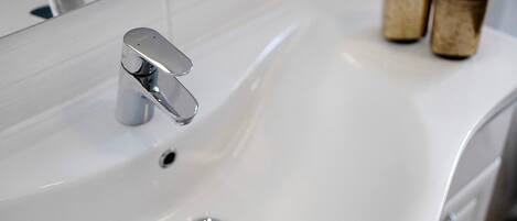 Un lavabo blanc dans une salle de bain, doté d'un robinet moderne et d'un miroir au-dessus.