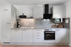 Una cocina moderna con armarios blancos, microondas integrado, cafetera y estufa.