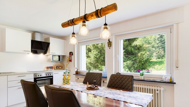 Una cocina moderna con armarios blancos, una mesa de comedor de madera y un amplio ventanal con vistas a la vegetación.