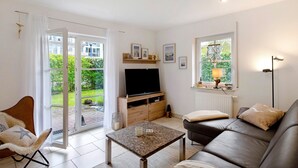 Een woonkamer met een bank, een salontafel, een televisie en een raam met uitzicht op groen.