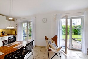 A kitchen with cabinets, a dining table, and chairs. There is a clock on the wall and a chair with a star pillow.