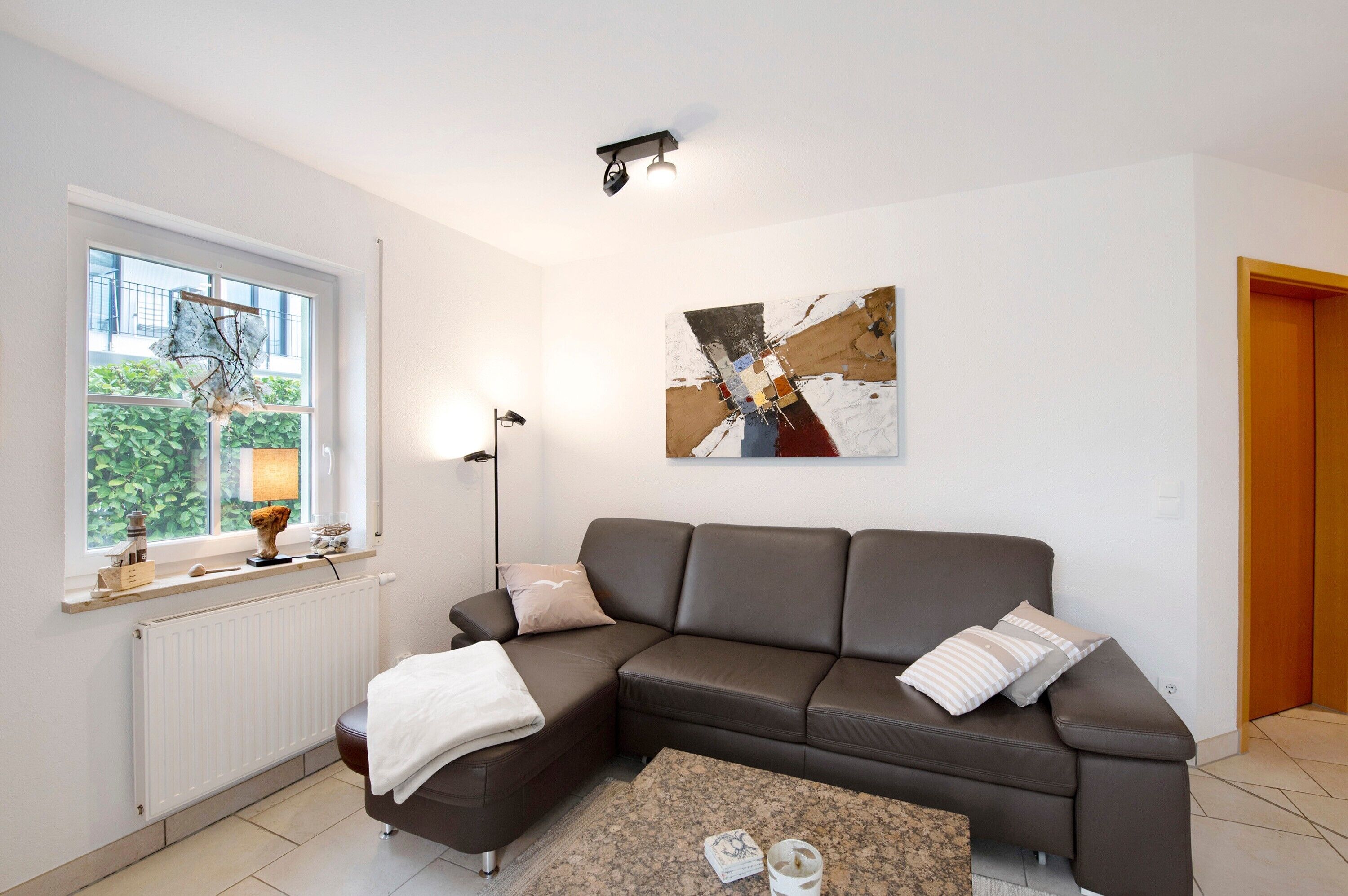 A modern living room with a sectional sofa, a coffee table, a floor lamp, a window with a view, and a piece of abstract art on the wall.
