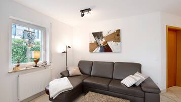A modern living room with a sectional sofa, a coffee table, a floor lamp, a window with a view, and a piece of abstract art on the wall.