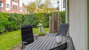 Een terras buiten met twee zwarte stoelen en een tafel, omringd door een haag en een gebouw op de achtergrond.