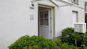 Een wit gebouw met een deur waarop '18b' staat, een klein raam en een stroomkast.