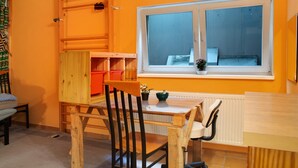 A room with a wooden table, a window with a view, a radiator, and a shelf with items.