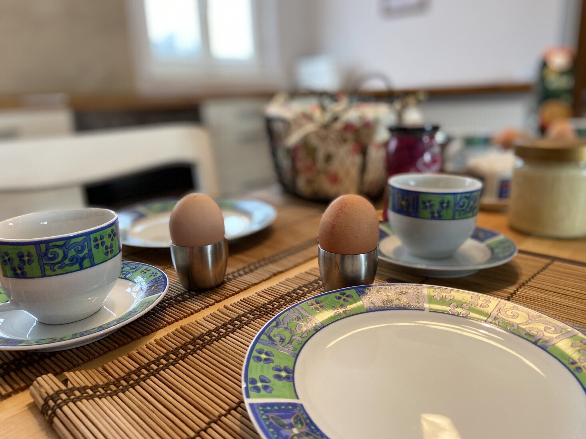 Een eettafel met een bord, twee eierbekers en een beker met een bloemenmotief.