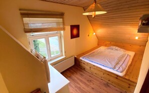Una camera da letto con soffitto in legno, una finestra con persiane, un letto con coperta a righe blu e bianche e un lampadario fissato al muro.