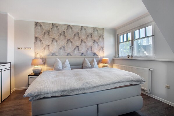 A bedroom with a large bed, two bedside tables with lamps, a radiator, and a window with a view.