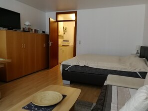 A compact room with a bed, a wooden wardrobe, a small table with a mat, and a television on a stand. - Studio Apartment 'Schloss Grubhof Appartement' with Balcony and Wi-Fi (Sankt Martin bei Lofer)