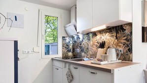 Una cocina moderna con armarios blancos, una ventana con vistas a la vegetación, una encimera con un hervidor y un salpicadero con diseño.
