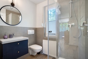 A modern bathroom with a glass shower enclosure, a white toilet, and a dark blue vanity with a mirror.