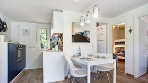 Una cocina moderna con armarios blancos, un comedor con mesa y sillas blancas, y vistas al exterior a través de una ventana.