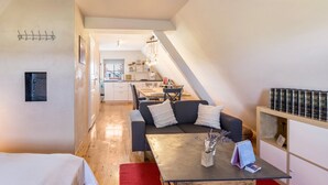 A modern, compact living space with a dining area, a sofa with cushions, a coffee table, and a bookshelf.