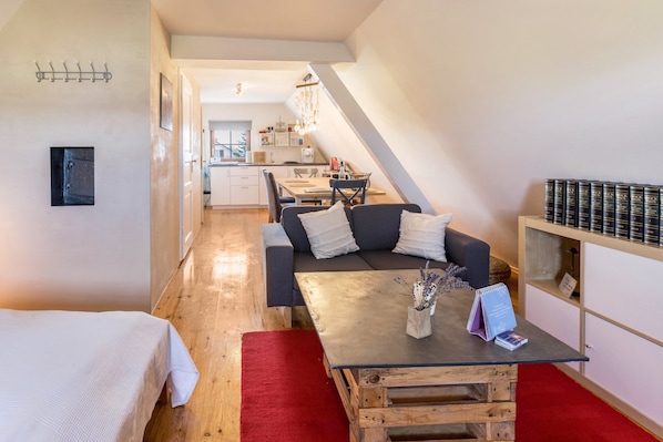 A modern, compact living space with a dining area, a sofa with cushions, a coffee table, and a bookshelf.