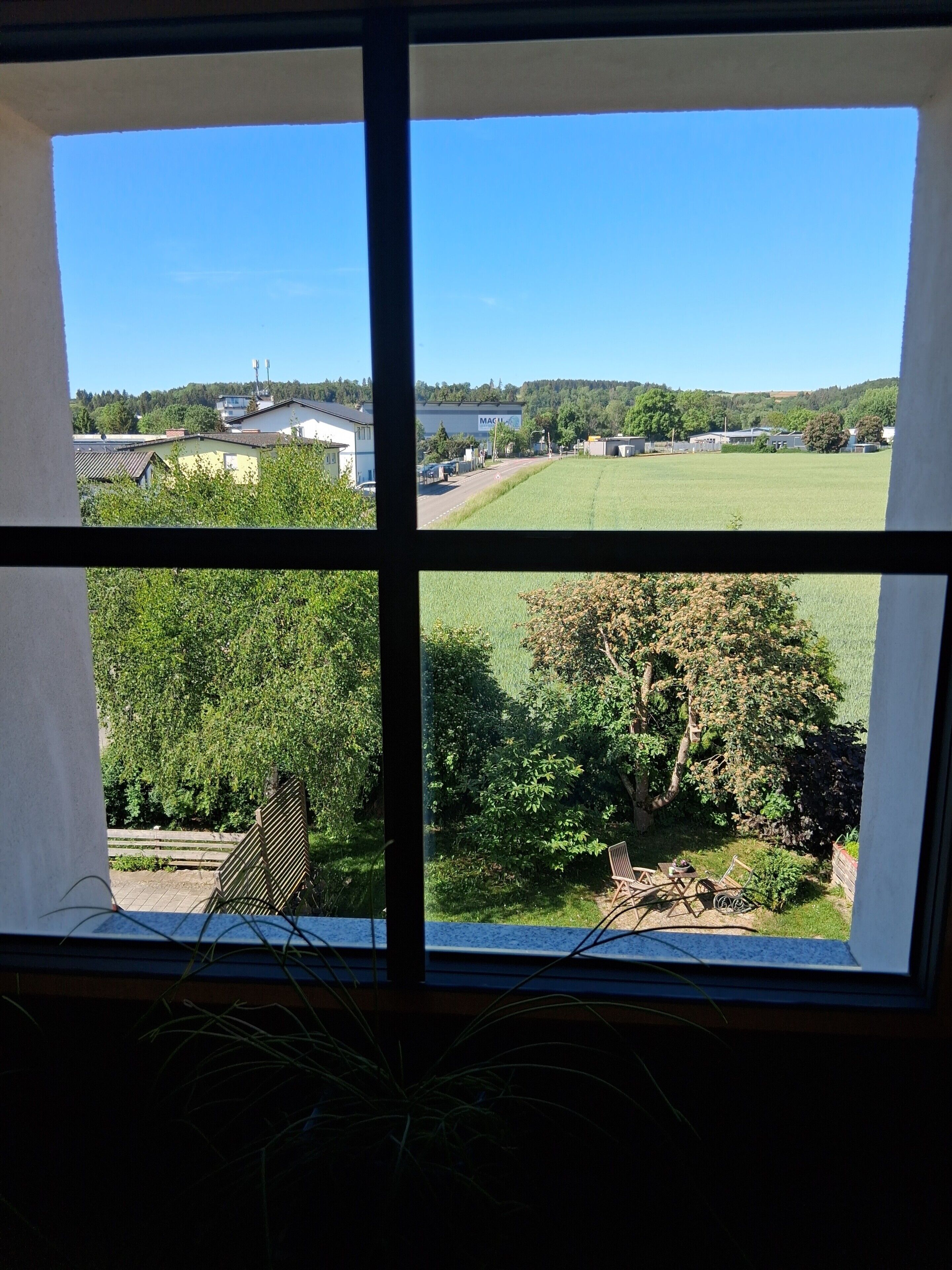 Una ventana que ofrece vistas a un paisaje rural, con casas, un campo y árboles.