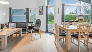 En moderne stue med en sofa, et spisebord og stole. Der er et stort vindue med udsigt til det fri.