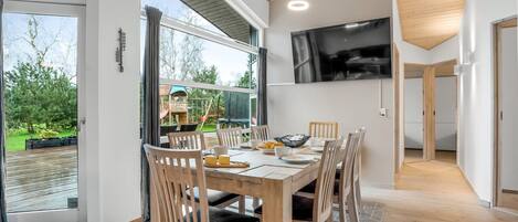 A modern dining area with a large table, wooden chairs, and a TV mounted on the wall.