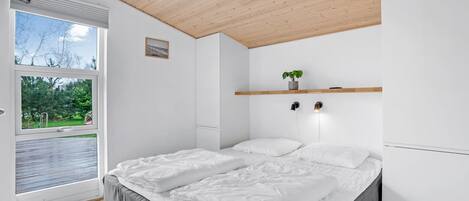 A bedroom with a large bed, a wooden ceiling, and a window with a view of greenery.