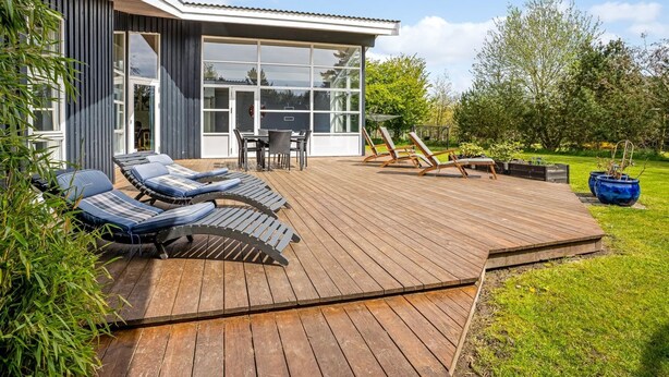 Et moderne hus med træterrasse, udendørs møbler og en glasdør, der fører til en patio.