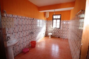 A bathroom with a sink, toilet, and shower area, featuring patterned tiles and orange walls. - Rufina Royal Lachung (Chungthang)