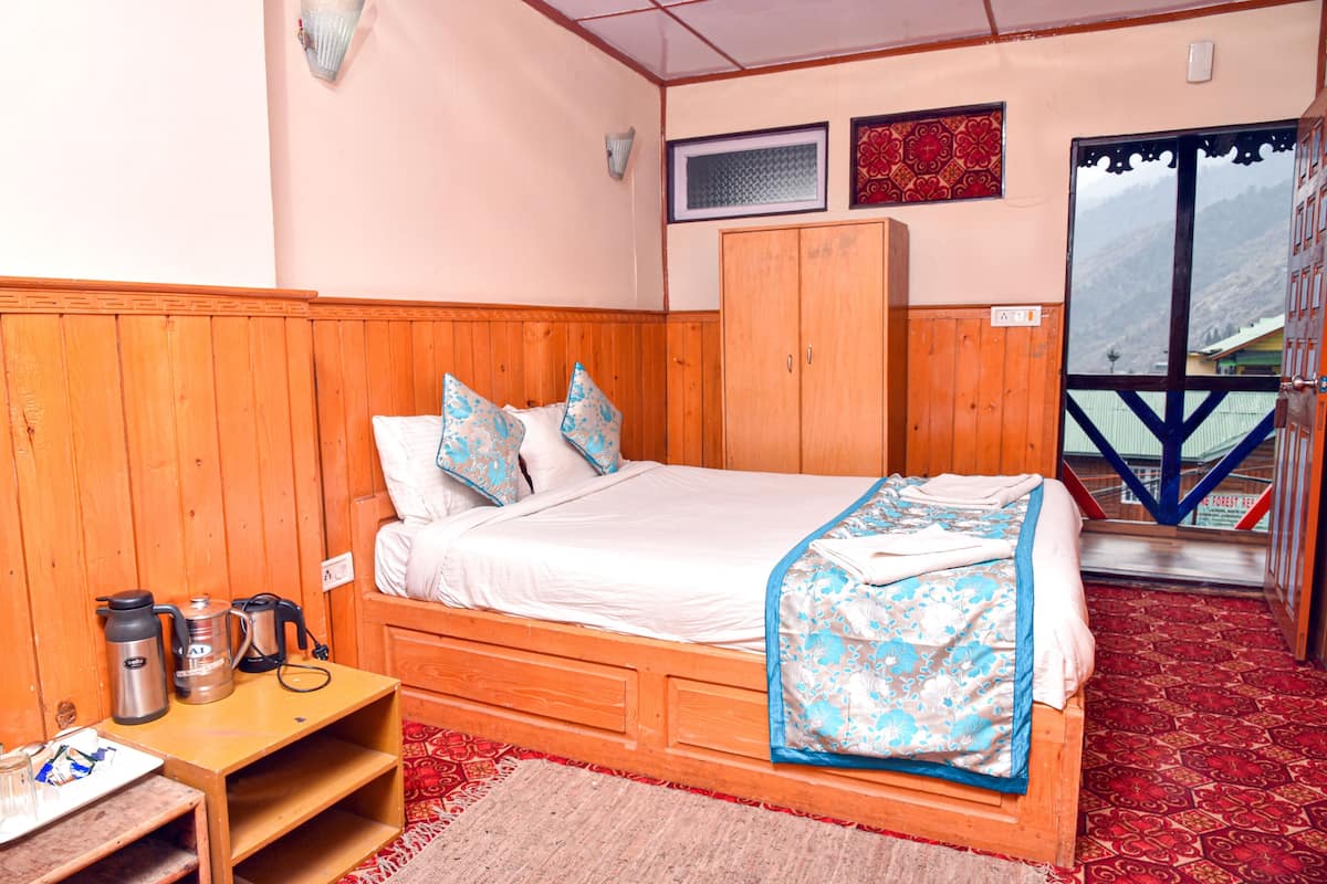 Une chambre avec un lit en bois, des oreillers, une table de chevet avec une bouilloire, et une vue sur les montagnes par la fenêtre.