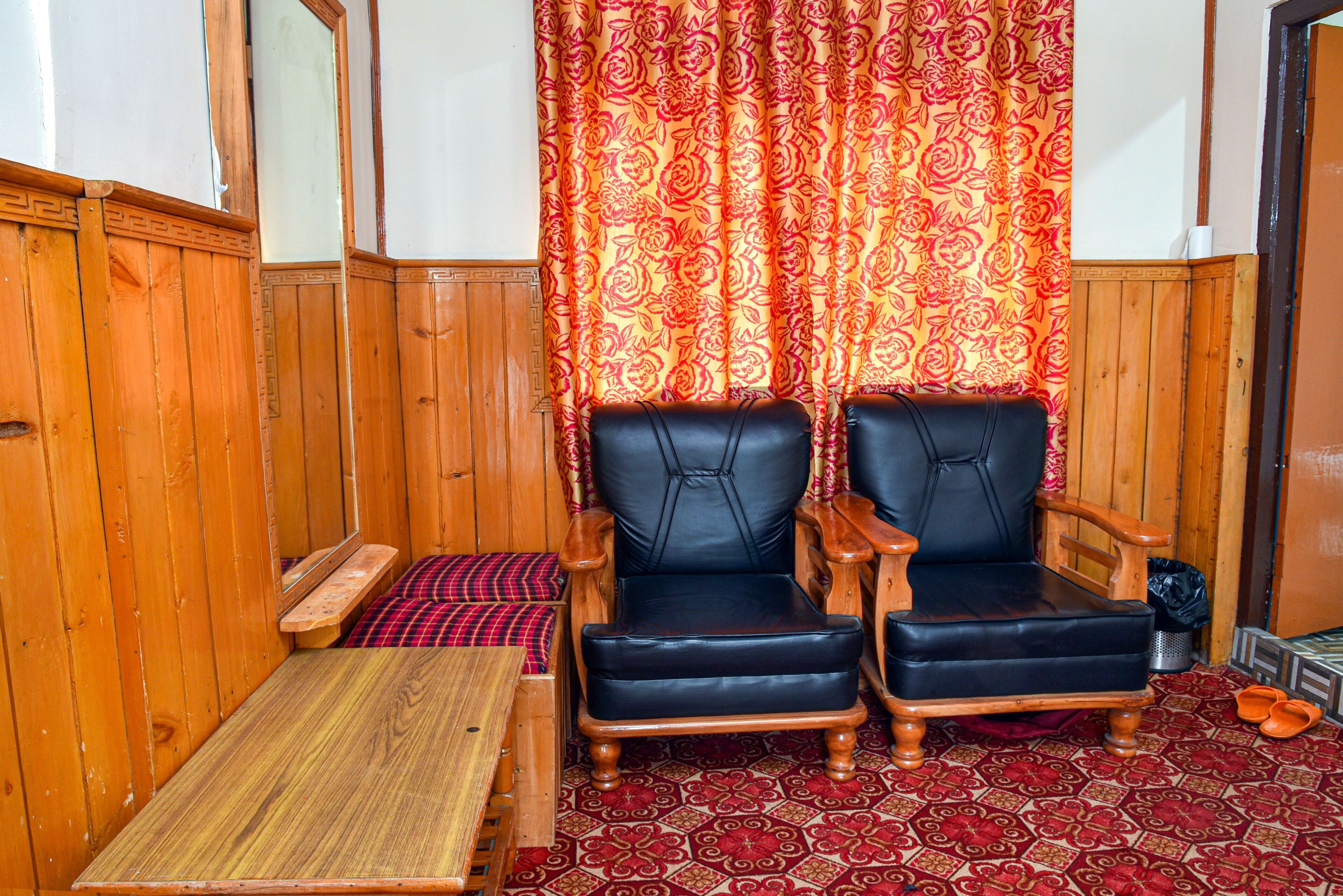 Ein Zimmer mit Holzvertäfelung, zwei schwarzen Ledersesseln, einer Holzbank und einem roten Teppich mit Muster.
